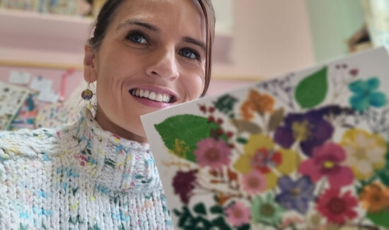 A photograph of designer maker Amber Marie in her Art Studio Holing one of her Pressed Flower Artworks