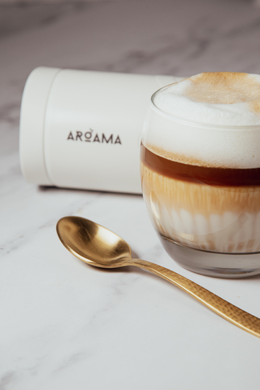 Portable espresso machine on a kitchen counter next to a cup of coffee and golden spoon