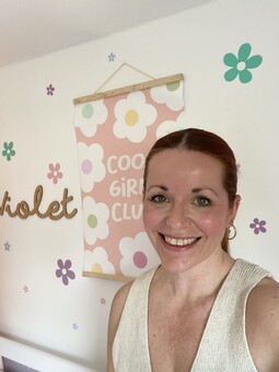 A photograph of the owner of Bunny and Bear Studio in front of a white wall with colourful pastel flower wall stickers and a 'cool girls club' hanging picture