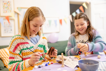 Image shows two children taking part in a craft activity at a birthday party. The children are painting wooden peg doll craft kits. 