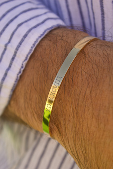man wearing a gold cuff bracelet with roman numerals engraved onto it.