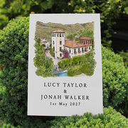 A painting placed on top of a green plant. The painting is of a building with text below.
