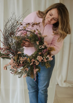Lynne looking down at a wild and rustic dried flower wreath in peach, yellow and green flowers