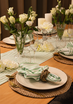 Green stripe napkin and table runner on a table with vases filled with white roses. 