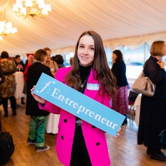Lauren, the founder of Luminosity Glitter in a pink blazer holding a f:entrepreneur sign.