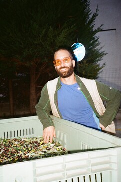a man smiling with orange glasses in front of a pile of olives