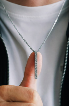 Man wearing a necklace with coordinates engraved. Showin the camera the text
