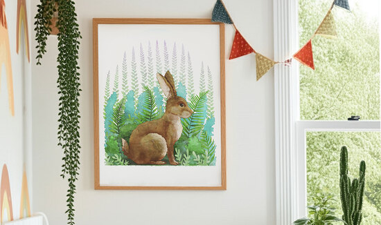 Framed woodland animal art print of rabbit in colourful children’s room with nursery bunting, plants, and large window showing garden greenery